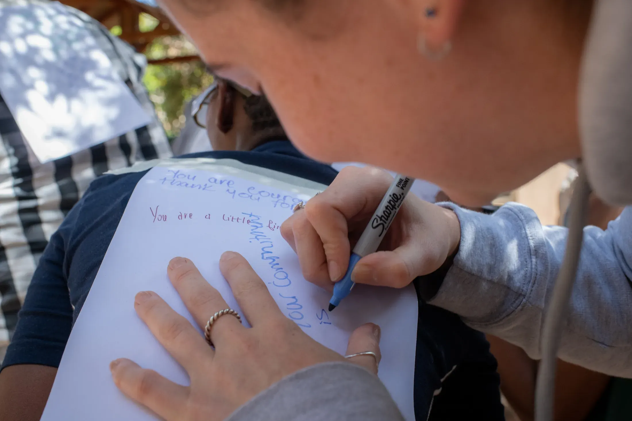 A participant writing a message in marker on a sheet of paper held against another person's back.